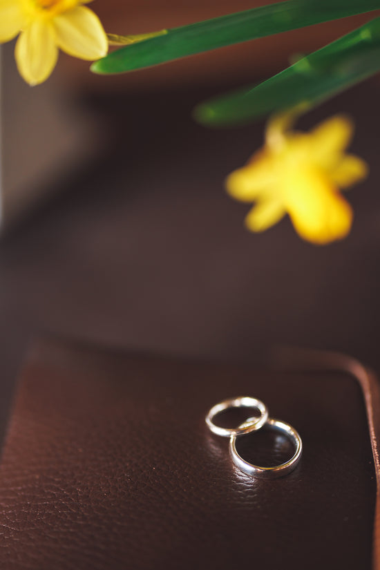 Couples white gold wedding bands on a leather photo book with a yellow flower at pulteney court wedding venue